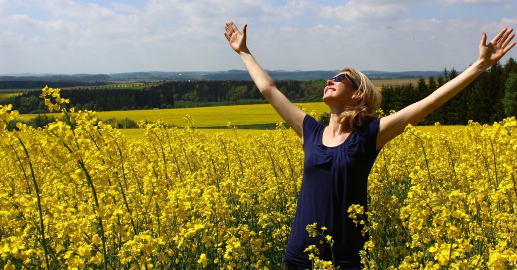 woman in field with arms raised in thanks