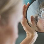 Woman looking into cracked mirror