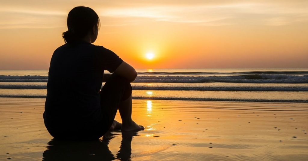 woman sitting on beach at sunrise