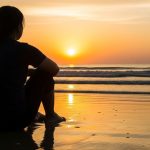 woman sitting on beach at sunrise